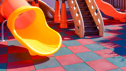 Slides with playground climbing equipment on colorful checkered rubber floor in outdoors playground area at kindergarten - obrazy, fototapety, plakaty