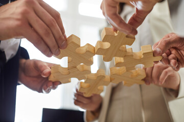 Team of business people joining parts of jigsaw puzzle. Closeup shot. Close up hands holding wooden pieces. Teamwork, connection, partnership, strategy, solution concept