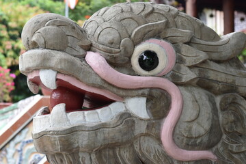 The head of a concrete dragon statue with a pink mustache and a red orb in its mouth.