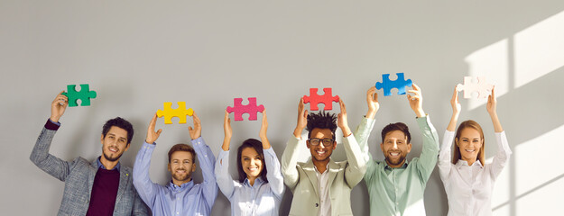 Business team with puzzle pieces. Group of happy multiracial people standing by grey office wall...