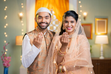 Happy indian muslim couple wishing for ramadan festival by saying with hand gesture by looking at camera - concept of islamic festival, togetherness and festive greeting. - obrazy, fototapety, plakaty