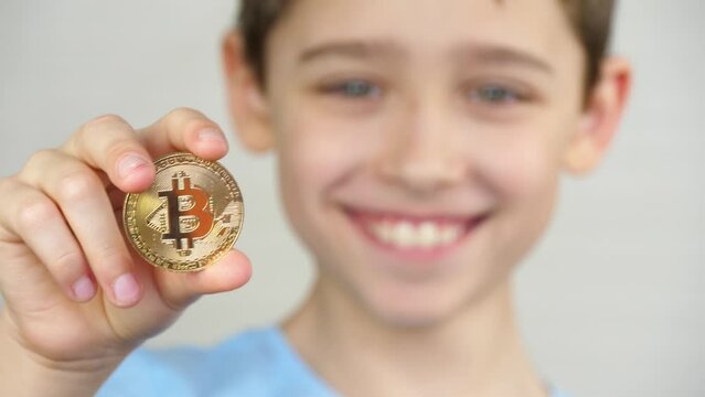 A man holds a crypto with a gold bitcoin. A face in the background. Child holding bitcoin. Concept of economic education in children.