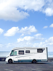 One modern motorhome parking on the asphalt against a blue ocean and sky. Concept of travel and living off grid people.