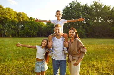 Zelfklevend Fotobehang Happy family spending time in fresh green park or city garden, enjoying nature and having fun together. Portrait of mum, dad and children standing on green lawn, with beautiful trees in background © Studio Romantic