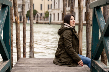 Fototapeta na wymiar Young female tourist sitting on a dock in Venice while taking in the scenery and enjoying her trip in the Italian city.