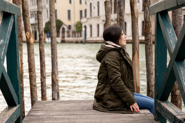Young female tourist sitting on a dock in Venice while taking in the scenery and enjoying her trip...