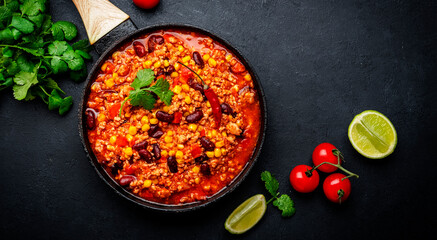 Chili con carne, mexican dish with minced beef, red beans, paprika, corn, cilantro and red peppers in spicy tomato sauce, tex-mex cuisine, black table background, top view
