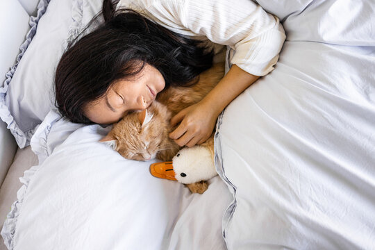 Young Asian woman with cute cat sleeping in bed