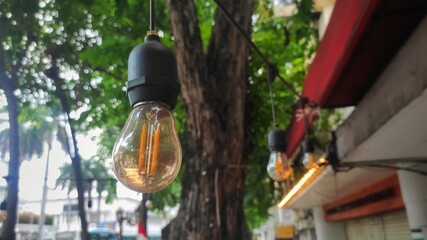 Yellow light bulb hanged on the pedestrian street near by tree to make the pedestrian street more...