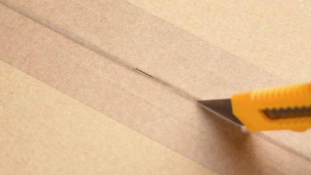 Person opening the received parcel cardboard box, cutting the paper adhesive tape with a sharp utility cutter knife close up