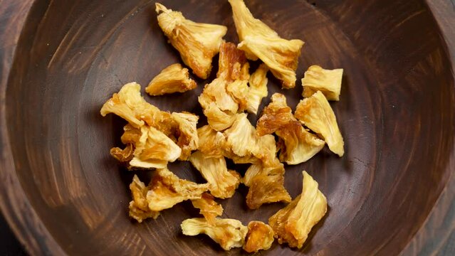 Pile of dried Pineapple chunks. Dehydrated organic yellow fruits in wooden rustic bowl close up. Rotation