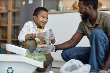 Portrait of smiling African American boy sorting plastic for recycling at home with father