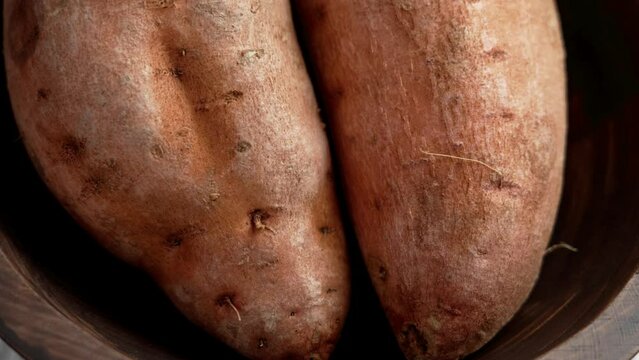 Whole sweet potatoes in a rustic wooden bowl. Uncooked raw yam roots. Fresh batatas. Rotation