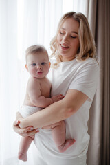 A 5-month-old baby and his  beautiful blonde mom relax, play and laugh in bed in the bedroom. People a dressed in light home clothes, the family chooses natural textiles