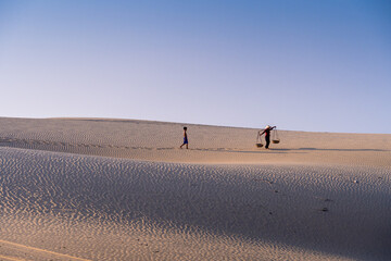 Fototapeta na wymiar Aerial view of a peasant woman carries a bamboo frame on the shoulder across sand dunes in Ninh Thuan province, Vietnam. It is one of the most beautiful places in Vietnam