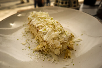 Holiday Napoleon cake or puff pastry cake with coconut chips and pistachio.On a glossy vintage plate. The restaurant style.Slice of multilayer Napoleon cake with butter cream.View from above. 