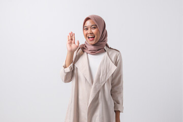 Portrait of attractive Asian hijab woman in casual suit raising hand, greeting and saying hi....