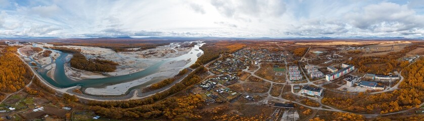 Autumn panoramic aerial view of the village and the river. Wide panorama. Beautiful rural landscape. Travel to Siberia and the Russian Far East. Klyopka village, Ola river, Magadan Region, Russia.