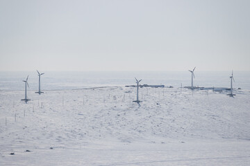 Winter arctic industrial landscape with wind power plant. Wind turbines in the snowy tundra on the coast. Wind generators. Renewable energy in the Arctic. Electric power and industry. Polar region.