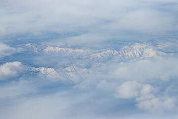 Top view of snow-capped mountains. Snow-covered mountain peaks among the clouds. Beautiful aerial landscape. Great for background. Khabarovsk region, Russia.