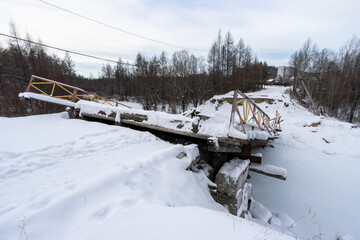 View of the collapsed road bridge. Collapsed bridge over a small river. Fallen damaged bridge. Consequences of an emergency. Cold winter weather. A lot of snow.