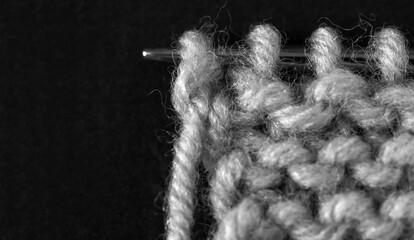 Close-up view of process of hand knitting warm gray wool scarf on metal knitting needle. Knitting as a hobby. Empty space for text on black background. Flat lay, copy space, macro, mock up