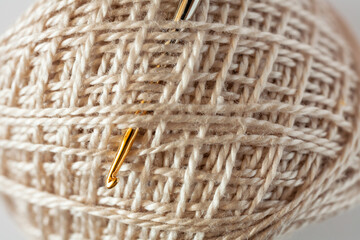 Close-up of skein of natural cotton light yarn and metal gold-plated crochet hook. The texture of cotton threads wound into a ball. Textile background. Crochet as a hobby. Flat lay, macro, top view