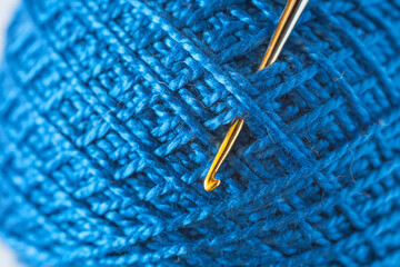 Close-up of a skein of blue natural cotton yarn and a metal gold-plated crochet hook. The texture of threads wound diagonally into a ball. Textile background. DIY concept. Flat lay, macro, top view