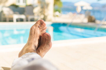 Barefoot male tourist relaxing by the outdoor swimming pool in seaside resort on sunny summer day