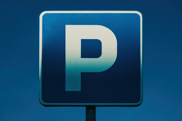 Parking area blue sign with white letter P illuminated by the warm sunset light