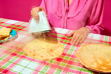 Woman in pink blouse ironing pancake on plaid tablecloth. Meme featuring unexpected ways to prepare food through humor. Concept of pop art, creativity, weirdness, food, humor, colorful photography - 772923637