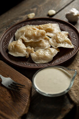 Dumplings in a clay plate with pepper and garlic sour cream sauce on a wooden table