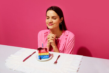 Happy young woman in pink shirt sitting at table with plate and birthday cake made of dishwashing...