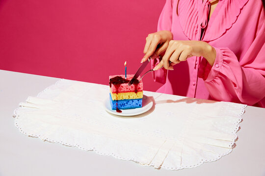 Cropped image of woman in pink shirt sitting at table and cutting birthday cake made of dishwashing sponges and candle. Birthday party. Concept of food pop art photography, creativity, quirky style