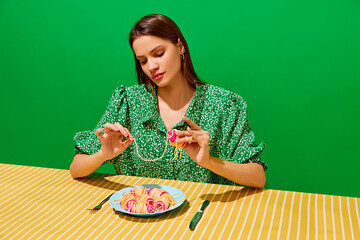Young woman spinning spaghetti on hair curlers against green background. Unusual presentation of food. Restaurant menu. Concept of food pop art photography, creativity, quirky style