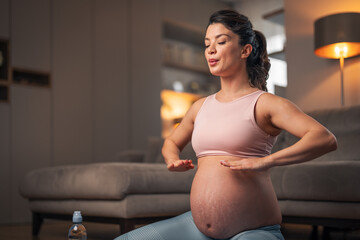 A focused young pregnant woman doing breathing exercises and meditating at home