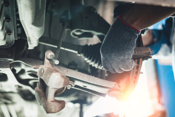 Auto mechanic in gloves fixing car suspension, under vehicle view with clear focus on hands and...