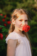 Portrait of beautiful young girl with red rose flower in her mouth while posing in the garden in summer. Children - Flowers Of Life. The charm of youth