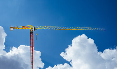A static construction crane pictured against a cloudy sky on a sunny day.