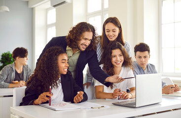 Group of high school students and classmates sitting in the classroom with male friendly smiling teacher and looking at the laptop monitor screen. Education and back to school concept.