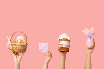 Female hands holding basket with eggs, Easter cake and gifts on pink background