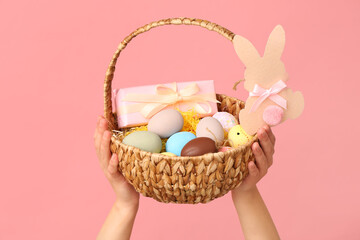 Female hands holding basket for Easter on pink background
