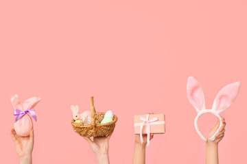 Female hands holding basket with Easter eggs, bunny ears and gifts on pink background