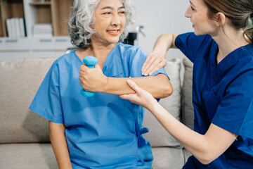 Physiotherapist helping elderly woman patient stretching arm during exercise correct with dumbbell in hand during training hand in hospital . in clinic