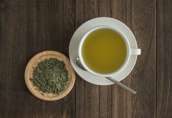 Green tea in white cup. Dry leaves of ground green tea on a small wooden plate