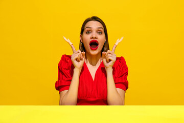 Woman in red dress with surprised expression, pointing upwards with toy hands against yellow background. Human emotions. Concept of food pop art photography, creativity, quirky style