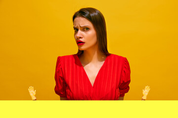 Woman in red shirt with surprised questioning expression, pointing upwards with toy hands against yellow background. Concept of food pop art photography, creativity, quirky style