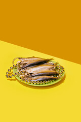 Smoked fish on a plate with pearl necklaces, on a diagonal yellow background, elegant arrangement....