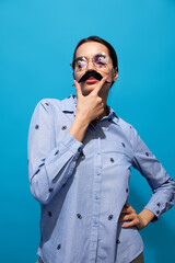 Young woman in shirt, wearing fake moustaches, glasses with eyes items on it and making funny...