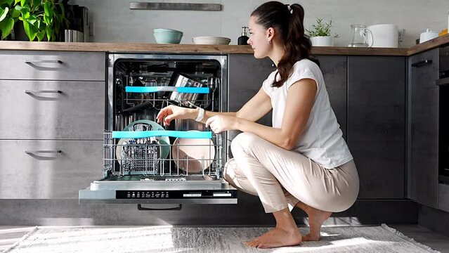 Young woman putting dirty ceramic dish in dishwasher. Household and helpful technology concept